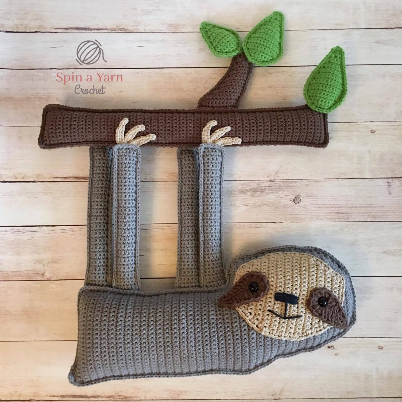 Finished crochet ragdoll sloth amigurumi lying flat on wooden table