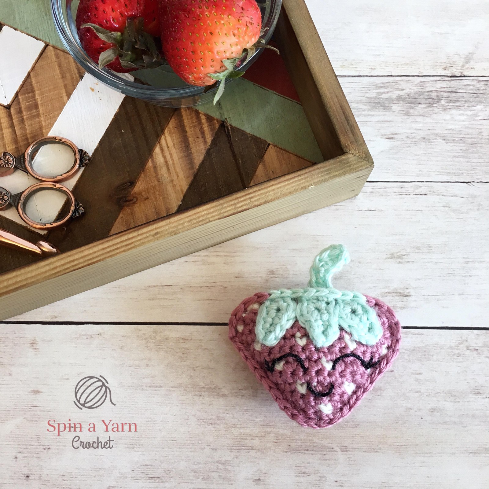 Crochet strawberry next to tray with bowl of strawberries