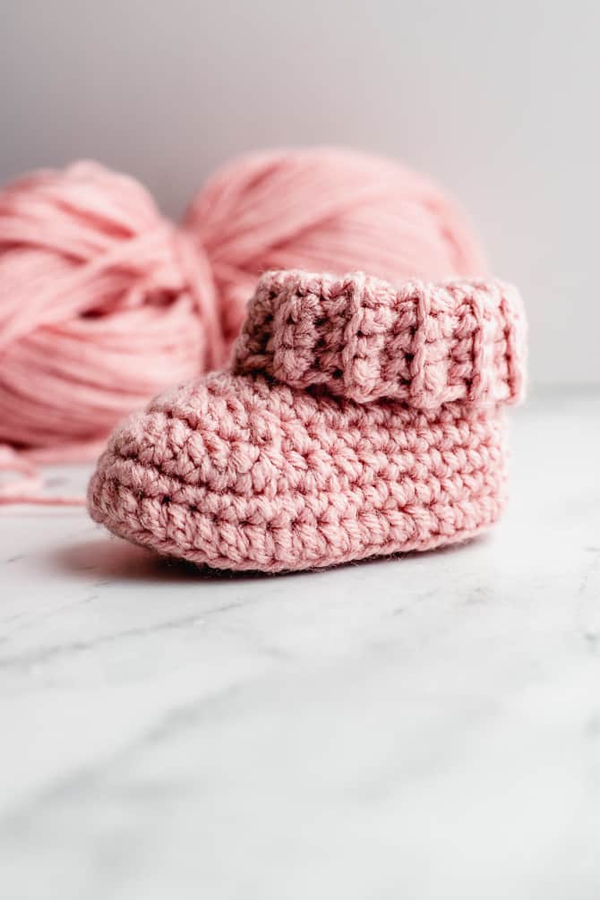 Pair of classic cream crochet baby booties with folded rib cuff on neutral surface