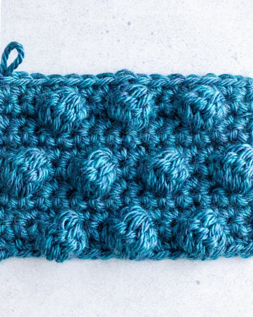 Crochet swatch featuring rows of raised 3D pink and cream bobbles popping off textured background