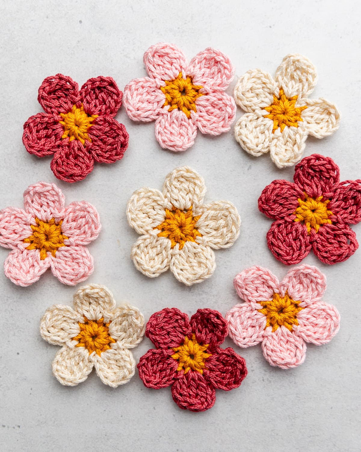Assortment of colorful pink and yellow crochet flowers on light gray background