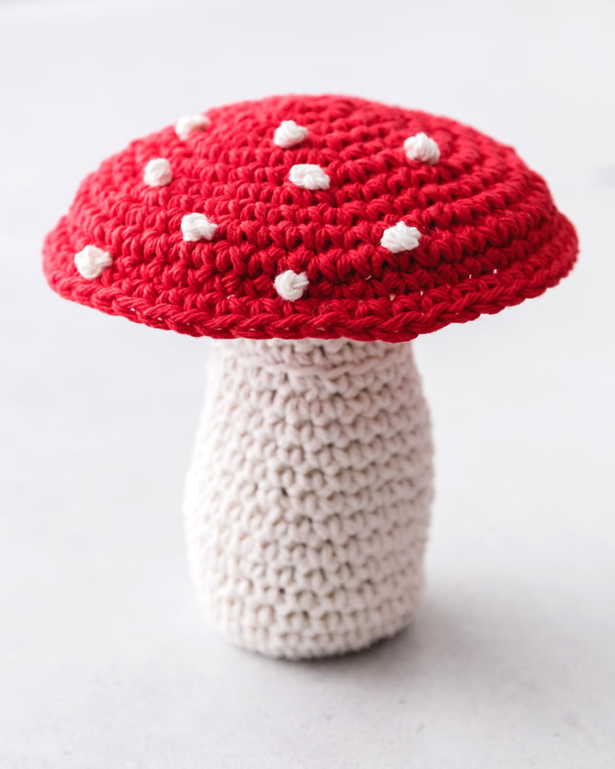 Adorable red and white spotted crochet amigurumi mushroom on moss display