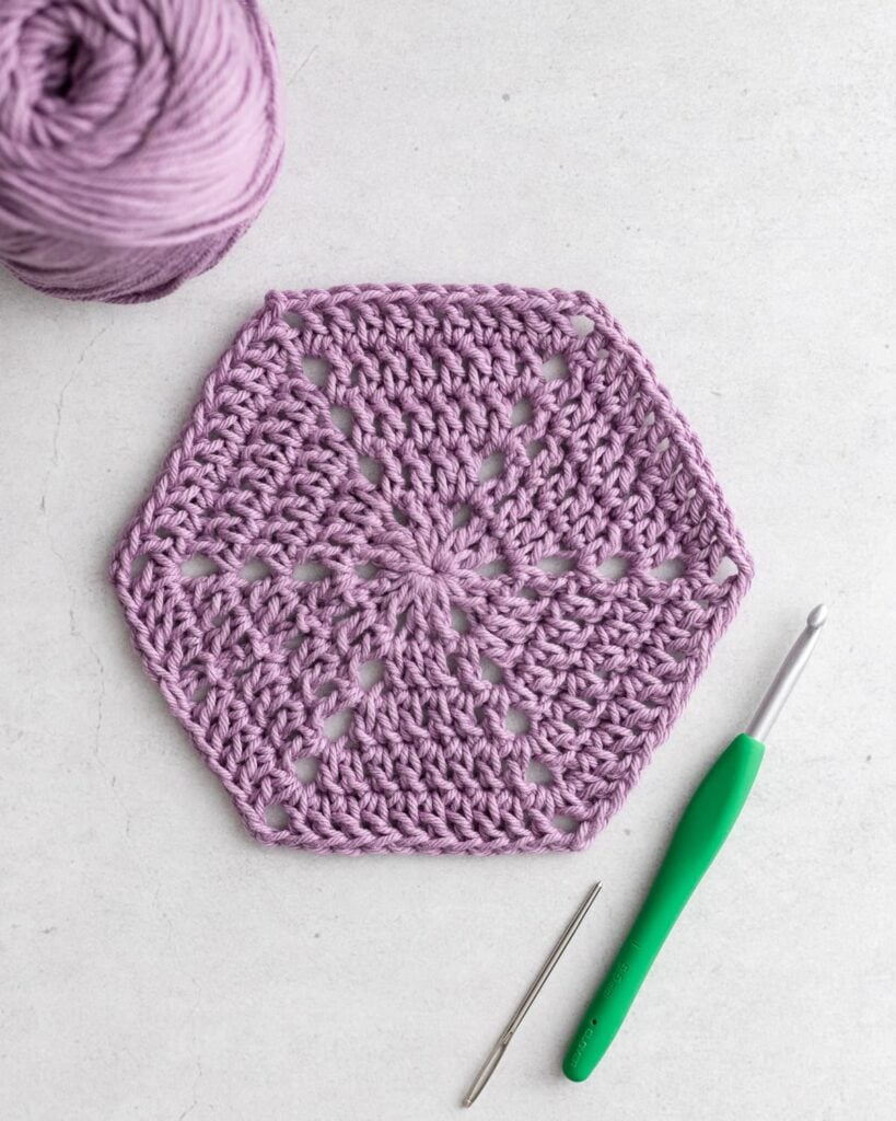 Handmade colorful crochet granny hexagon motif lying flat on rustic wooden craft table