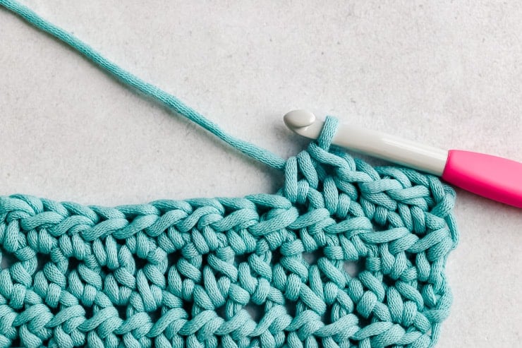 Clean swatch of half double crochet rows in warm oat acrylic yarn with ergonomic crochet hook