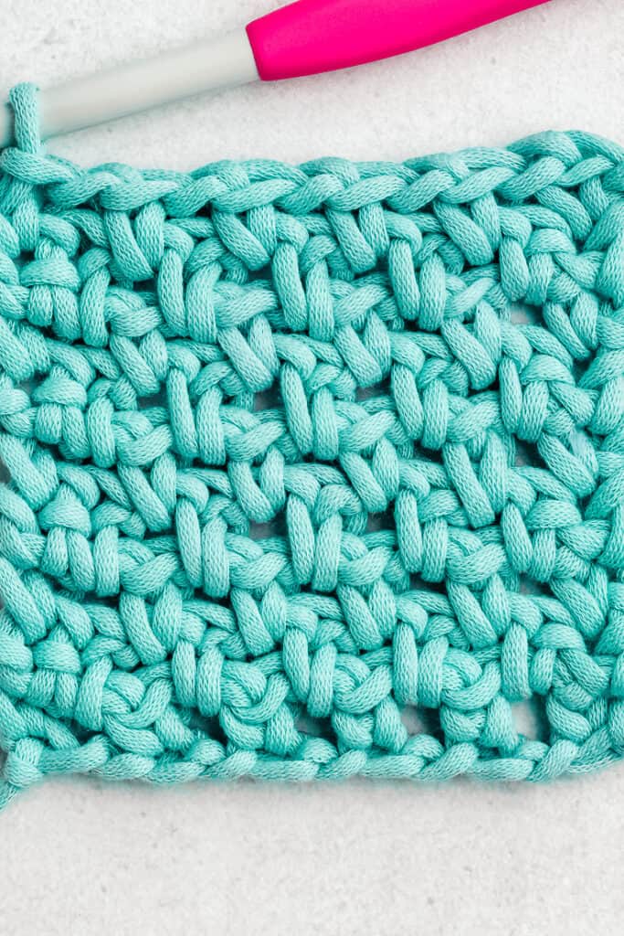 Clean woven textured crochet moss stitch swatch in gentle pastel tones with crochet hook