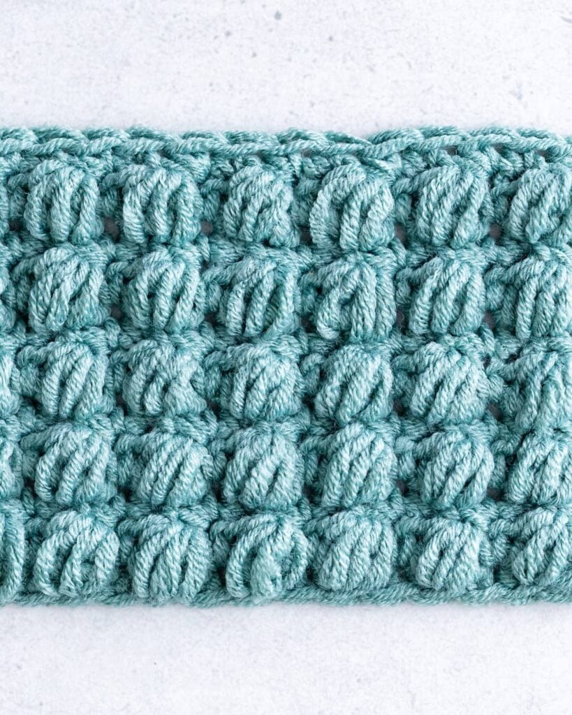 Row of fluffy golden mustard puff stitches crocheted into soft wool swatch with wooden crochet hook
