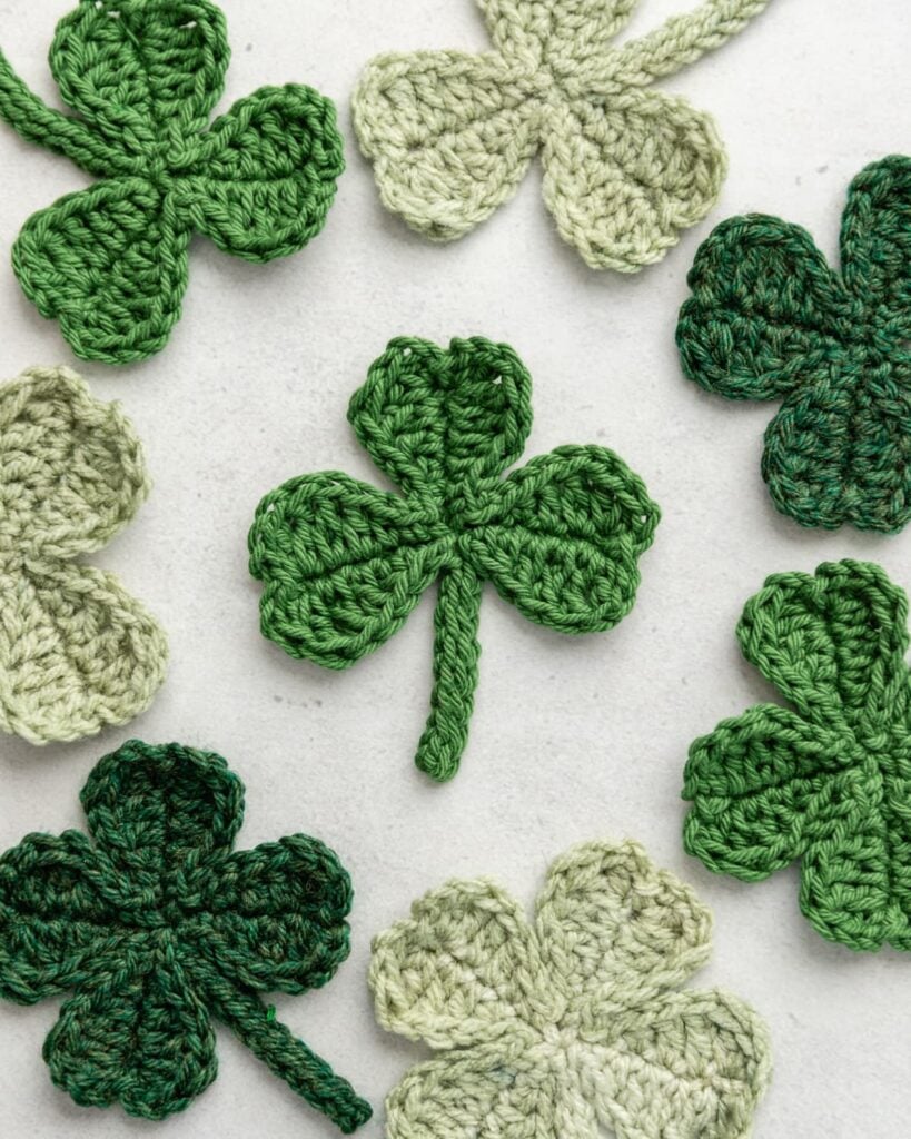 Trio of vibrant green crochet shamrocks and four-leaf clovers with curved stems on light background