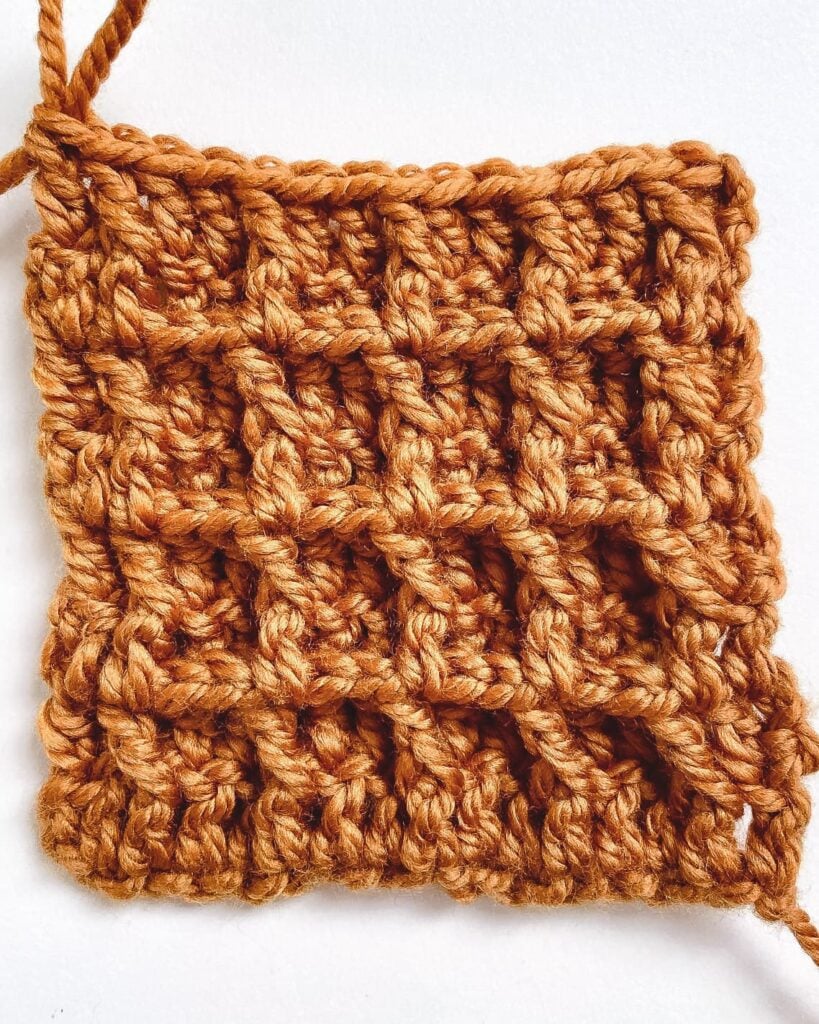 Thick squishy crochet waffle stitch swatch in cream textured yarn with crochet hook