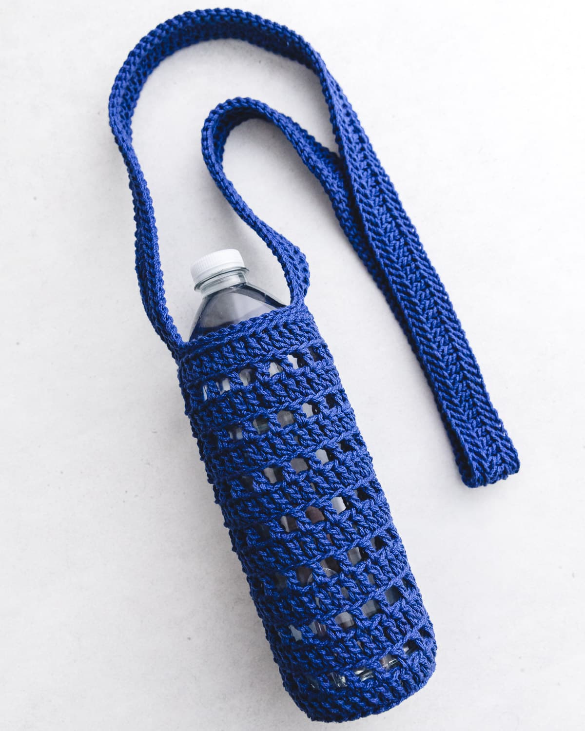 Blue cotton crochet water bottle holder with clear bottle flat on neutral background